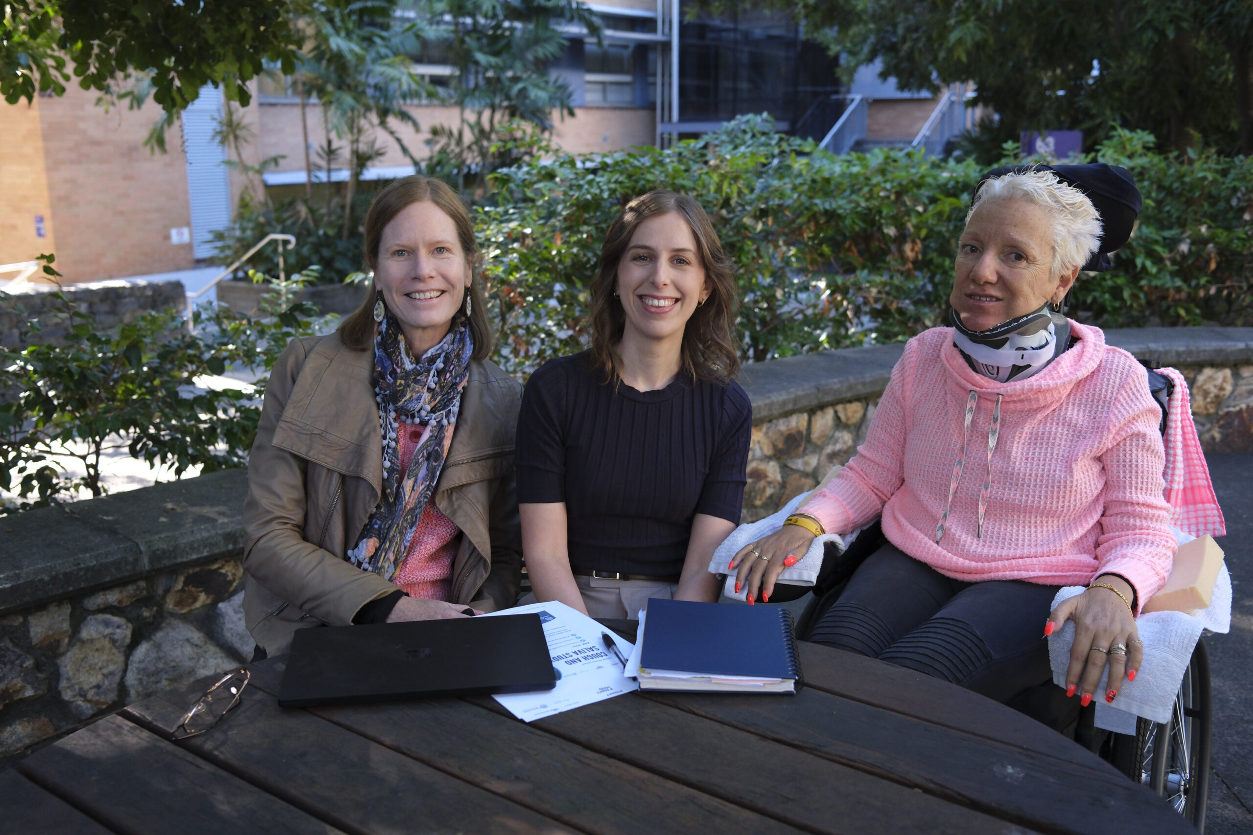 Researchers sitting with a MND patient. All looking at the camera and smiling.